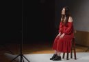 Martyna Sowińska. Dziewczyna w czerwonej sukience siedzi na krześle w studiu fotograficznym, śpiewa piosenkę